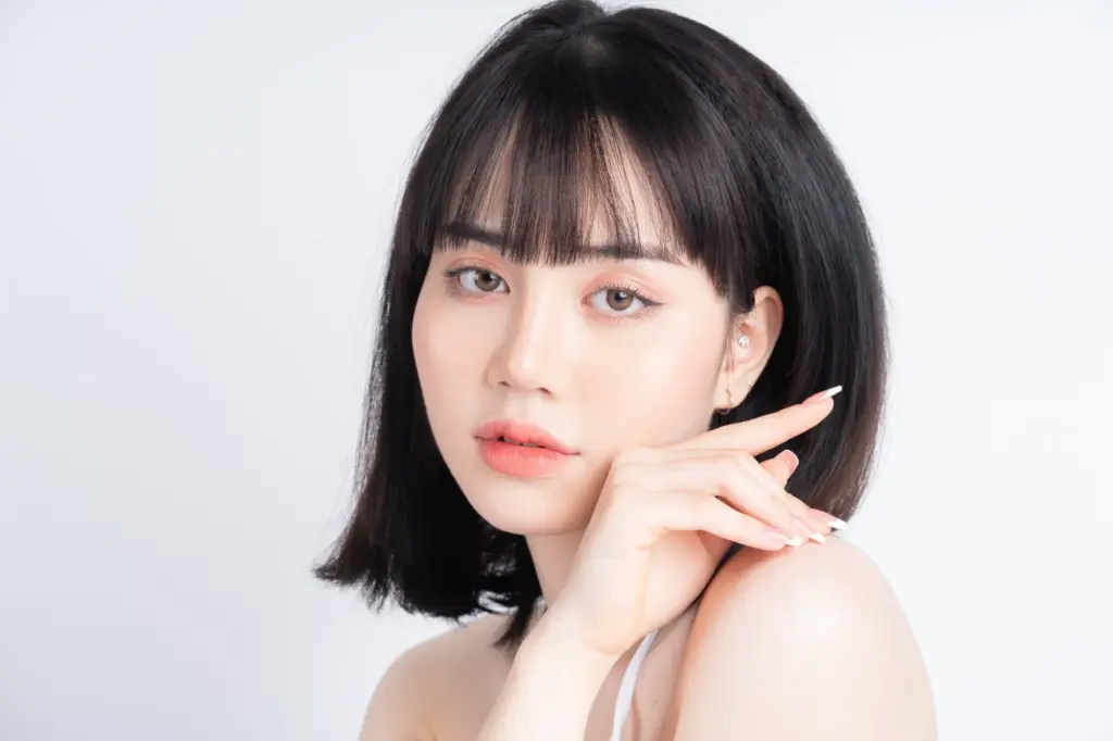 Woman with clear, smooth skin and soft makeup touching her face, representing professional facial treatments and skincare services for a radiant complexion.